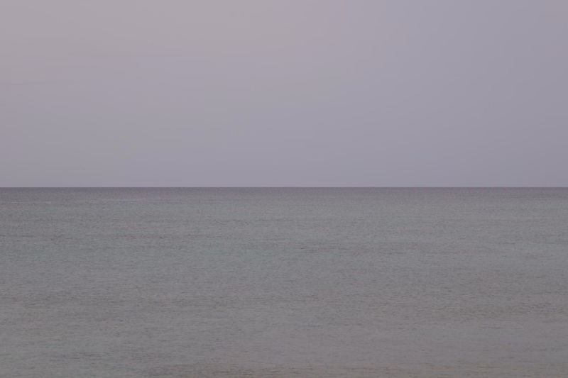 A vast, calm expanse of gray water meets a pale, featureless sky at the horizon.
