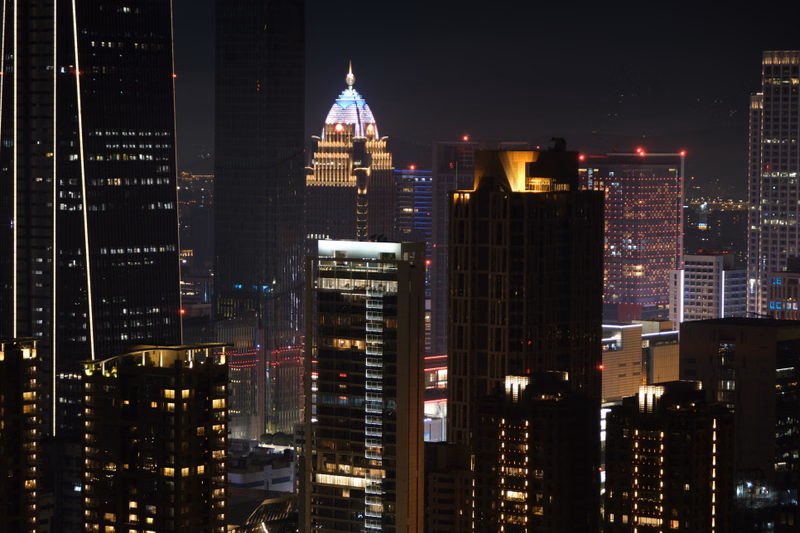 A nighttime cityscape view featuring numerous illuminated skyscrapers, including a prominent building with a dome.