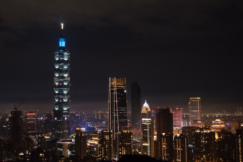 A nighttime cityscape featuring a prominent, brightly lit skyscraper tower against a dark sky.