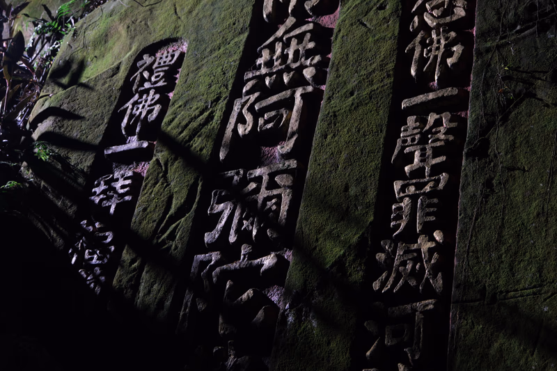 A serene and contemplative stone wall with engraved Chinese characters, illuminated by natural light, casting shadows on the wall.