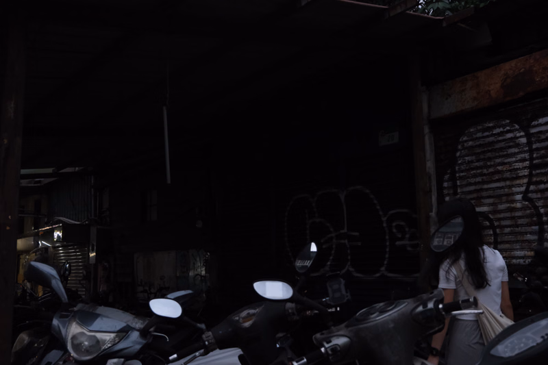 A person stands near several parked motorcycles in a dimly lit garage area with a corrugated metal door.