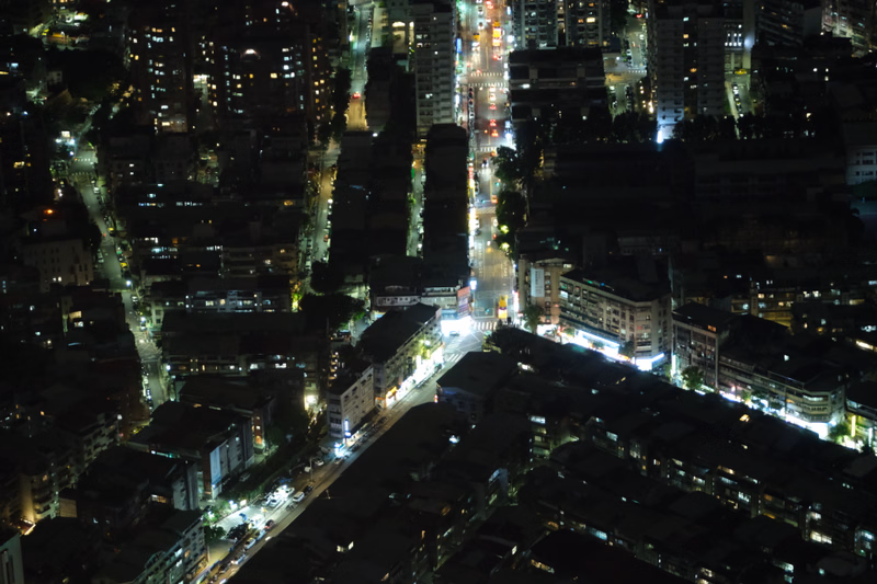 A nighttime aerial view of a dense urban cityscape with illuminated streets and numerous high-rise buildings.