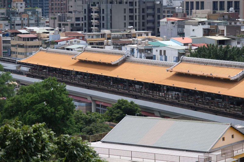 A view of a train station with long, orange-tiled roofs surrounded by dense urban buildings in a city.