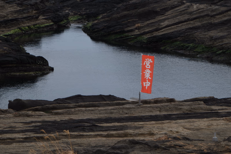 A red flag stands prominently in the rocky landscape near a body of water.