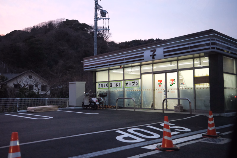 A Seven Eleven convenience store is shown at dusk, with a sign displaying "2月20日(木) オープン".