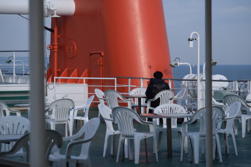 A red tower structure dominates a ship's deck with outdoor tables and chairs overlooking the ocean.