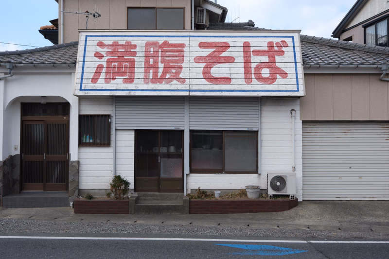 A storefront with a large red and white sign that reads "満腹そば" (Manpuku Soba) above the entrance.