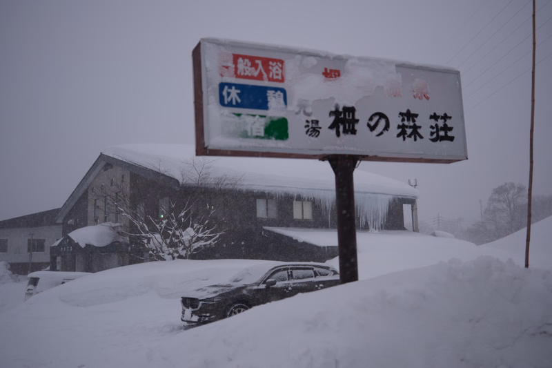 A white sign in the snow reads "散入浴 休 湯楓の森荘" in front of a low building.