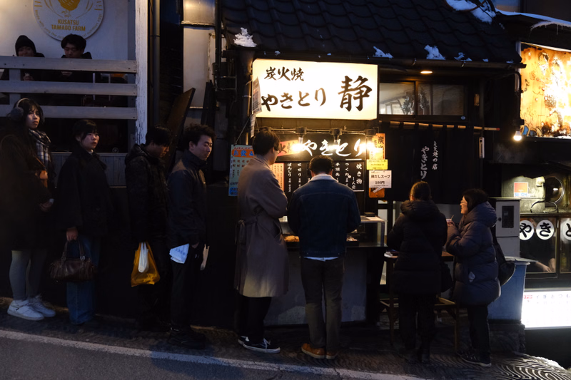 A nighttime photo of a restaurant with a sign that reads "炭火 やきとり 静" and several people gathered outside.