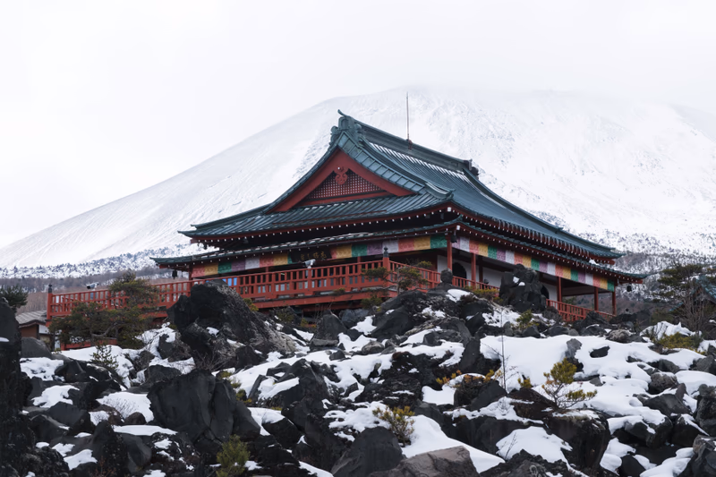 A traditional Japanese temple in a snowy landscape with a prominent mountain in the background.