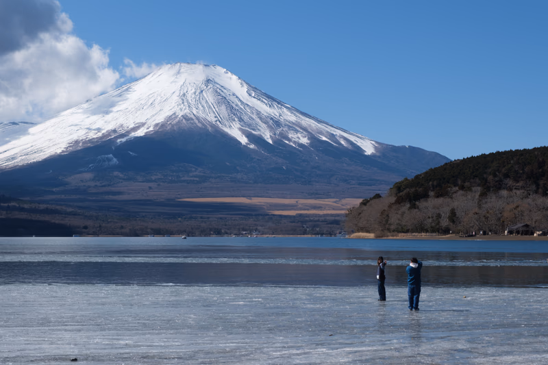A photo of a lake in front of a snow-capped mountain with two people standing in the water.