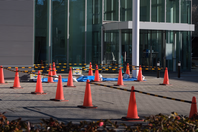 A construction site with red traffic cones and a building in the background.