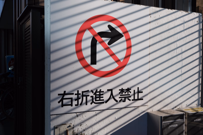A white sign with a red circle and a diagonal line over a right-turn arrow, and Japanese text reading "右折進入禁止" below it.