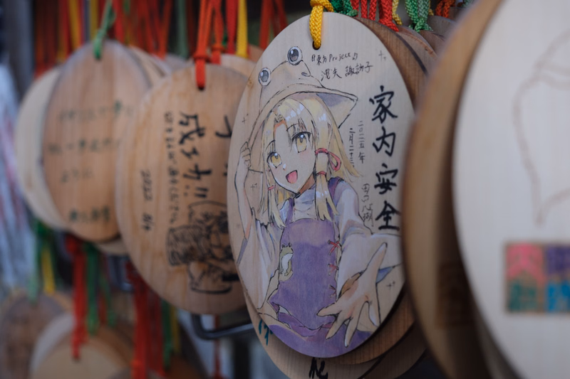 A round wooden print featuring an anime girl illustration with Japanese text that reads "家内安全".