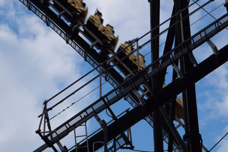 A large, dark roller coaster structure ascends against a cloudy blue sky.