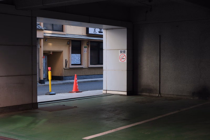 An entrance area with a white wall displaying a red and white sign that reads "禁煙" and several orange traffic cones.
