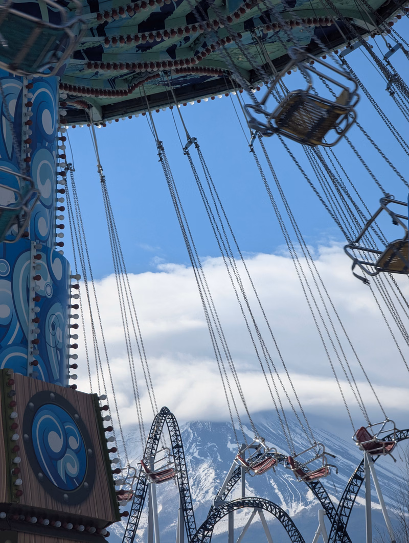 A view from a roller coaster ride looking down at the steel track against a backdrop of mountains and a blue sky.