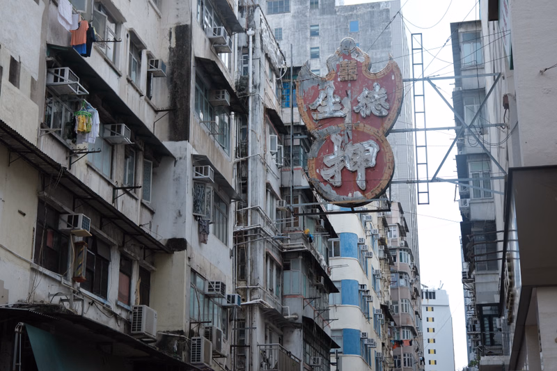 A large, ornate red and gold sign featuring Chinese characters is mounted on the facade of a dense urban building.
