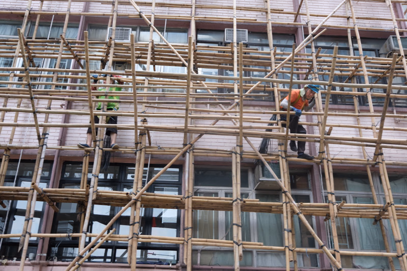 Workers are visible on a large wooden scaffolding structure surrounding a multi-story building under construction.
