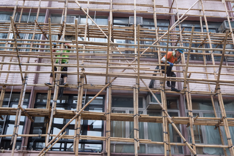 A worker is seen on scaffolding, performing a task on the exterior of a building.