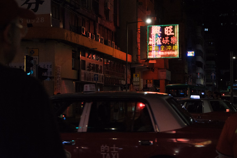 A red taxi is visible on a dark city street at night, with a bright neon sign displaying Chinese characters that read "無限幸福".