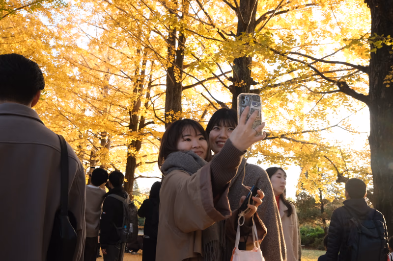 A photo of two people taking a selfie in a park with yellow leaves in the background.