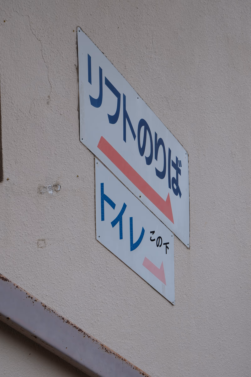 A ceiling sign with Japanese text and a smaller sign with a pink arrow and a red arrow pointing downwards.