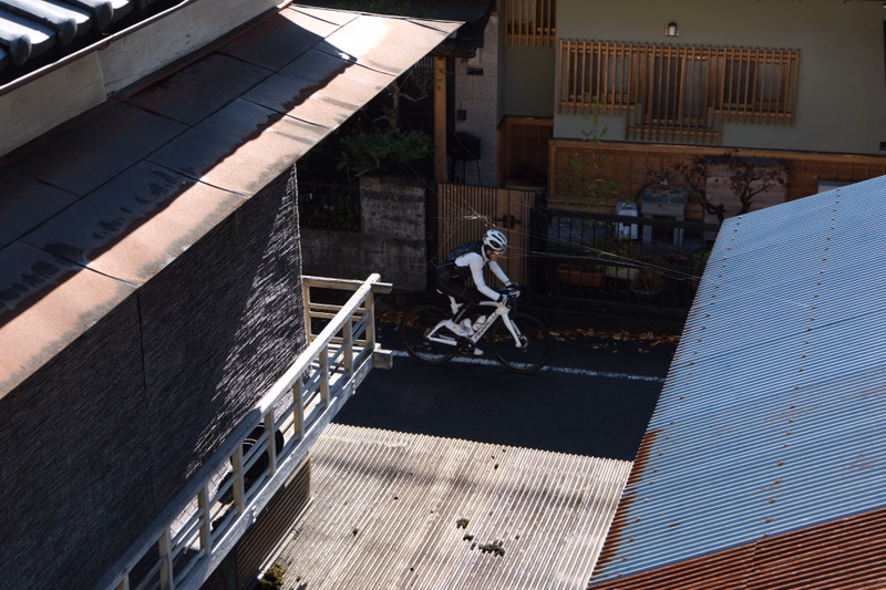 A cyclist rides a bicycle down a paved driveway between modern houses on a sunny day.