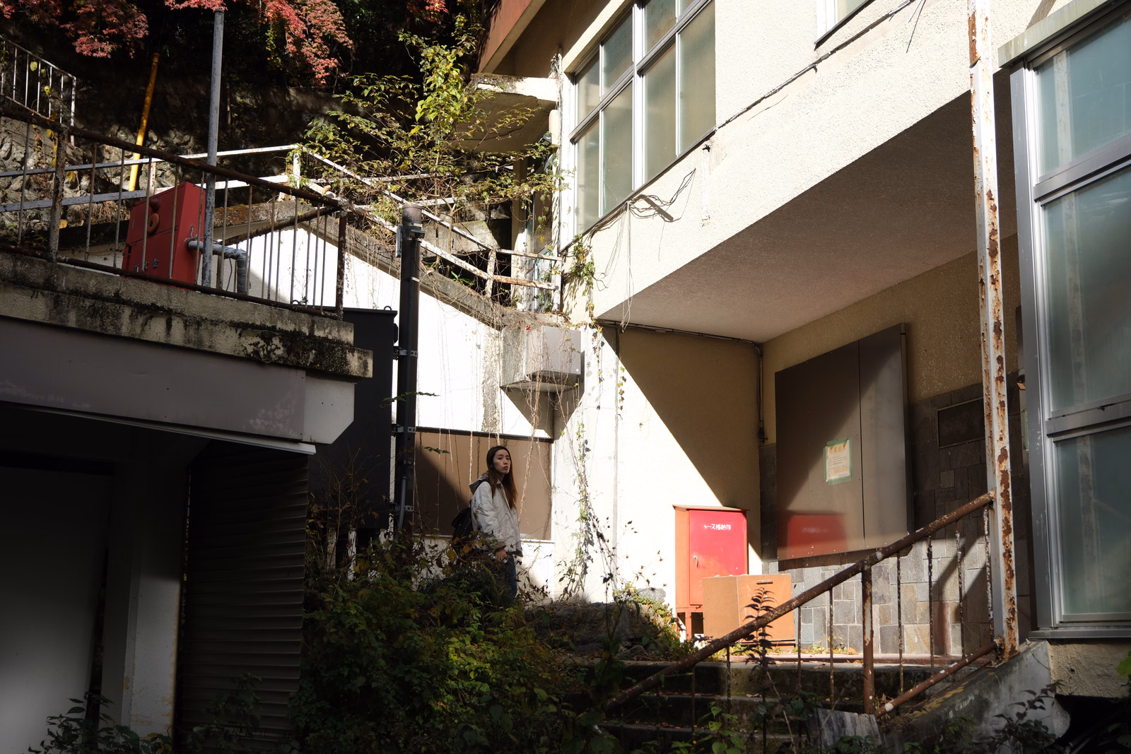 A person stands near a modern apartment building with outdoor stairs and a red mailbox visible on the ground level.