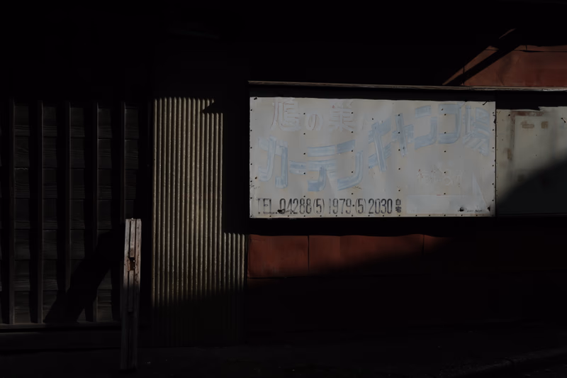 A photograph of a weathered signboard in an urban setting, casting long shadows on a building.