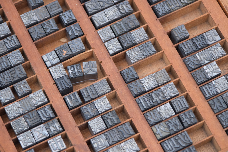 A collection of small, square wooden blocks engraved with Chinese characters, arranged in rows on a wooden tray.