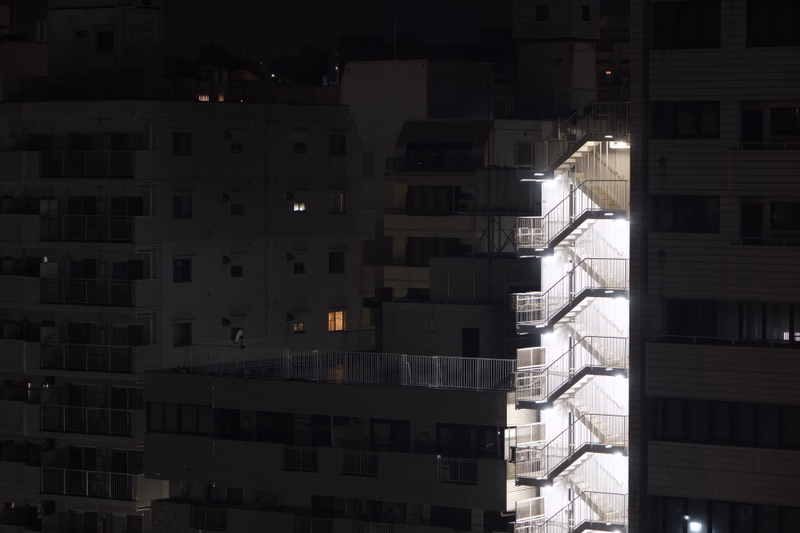 A metal external staircase is illuminated against the dark facades of several apartment buildings at night.