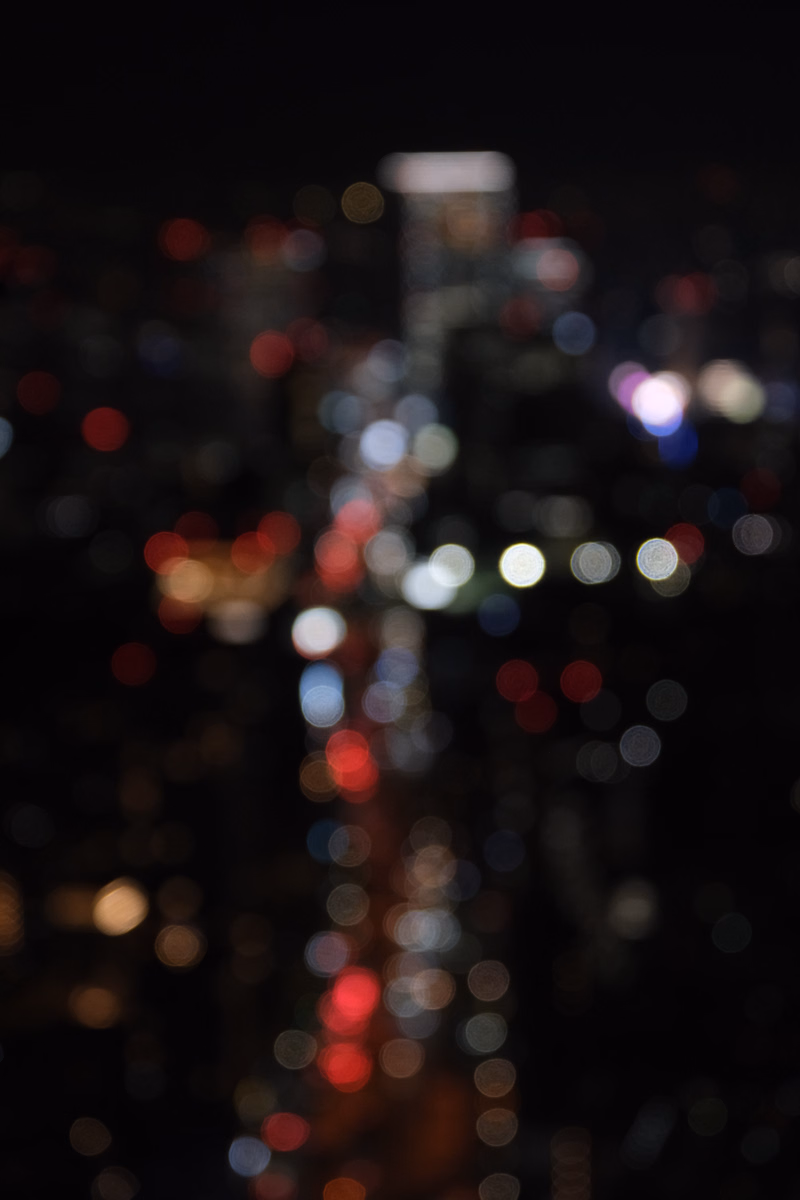 A blurred nighttime photograph showing numerous colorful bokeh lights from a city view.