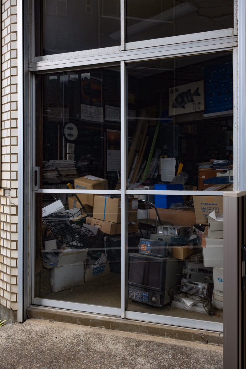 A photo of a glass door with a cluttered interior filled with boxes, a microwave, and a poster.