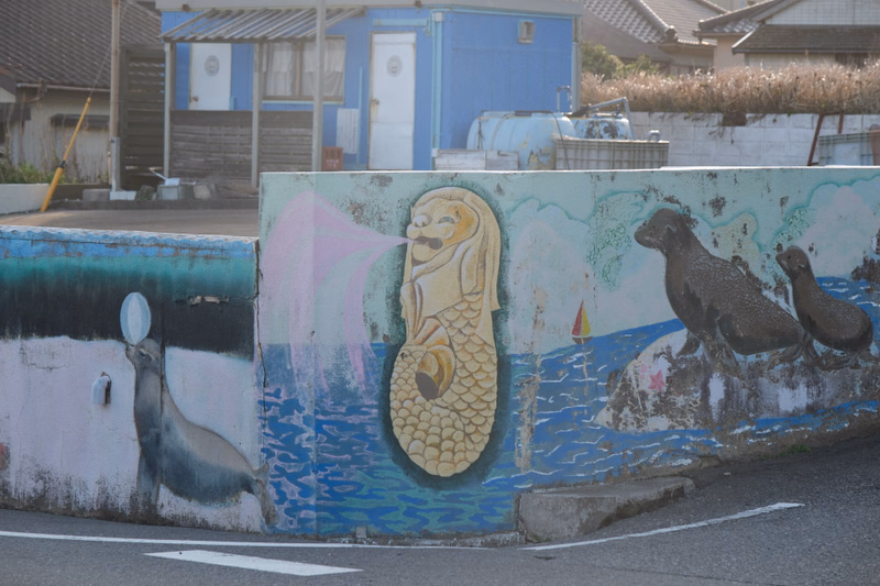 A colorful outdoor mural painted on a low wall features a sea turtle, a dolphin, and two dark fish.