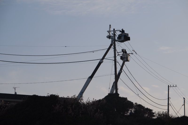 A utility pole with electrical equipment stands against a pale sky, with multiple power lines stretching across the frame.