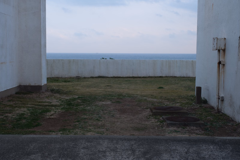 A view through a white structure overlooking a calm ocean under a pale sky.