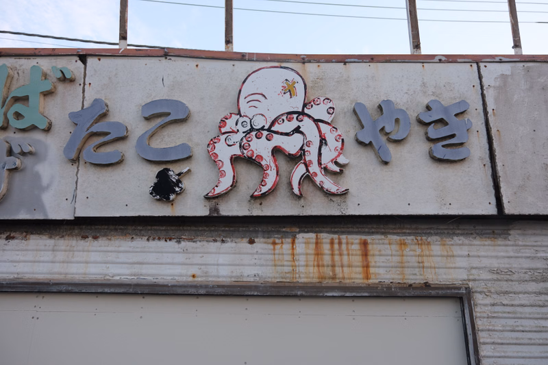 A weathered sign featuring a large octopus graphic and Japanese characters that read "はたこやき".