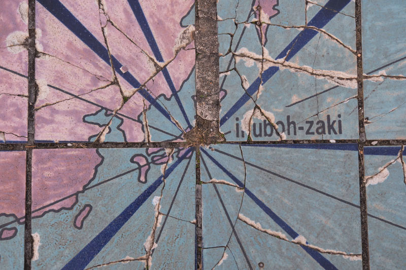 A cracked mosaic tile features a design with radiating lines and the legible text "i.uboh-zaki".