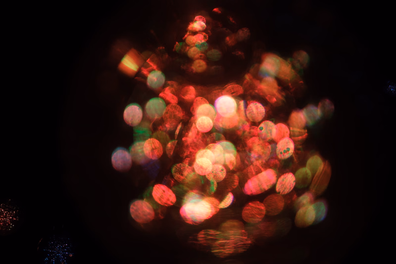 A dark photograph featuring a cluster of colorful, out-of-focus lights creating a bokeh effect.