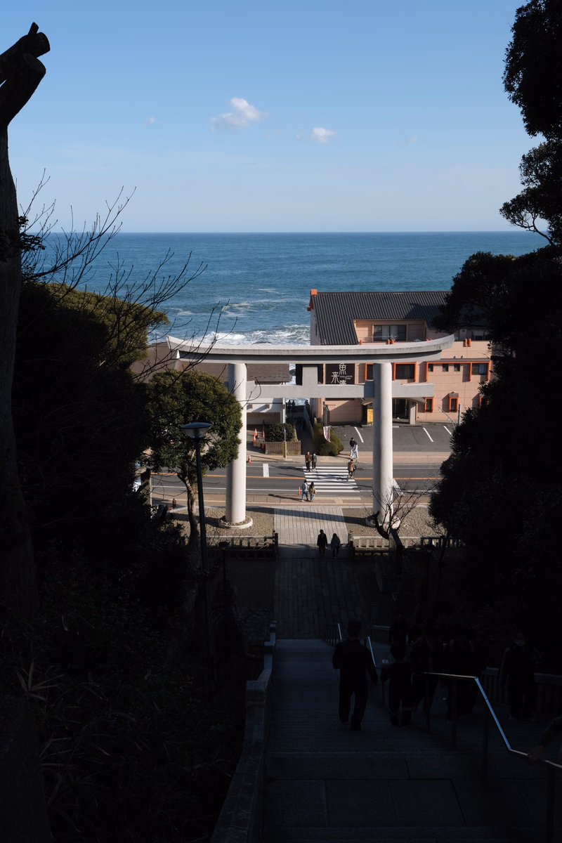 A view overlooking the ocean from a hillside, showing coastal buildings under a bright blue sky.