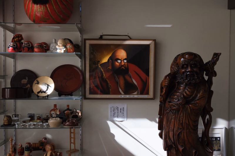 A dark wooden statue of a bearded man stands next to a framed portrait painting of a man with a beard on a shelf display.