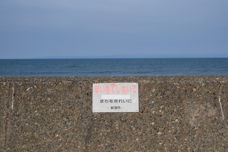 A sign on a concrete seawall reads "ほい潜れないで まちをきれないに - 新潟市 -" overlooking the sea.