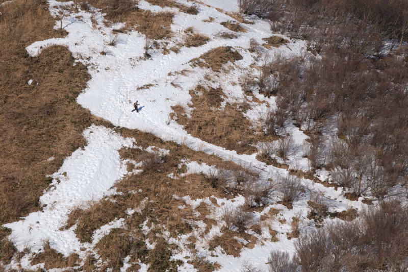 A person is visible walking along a winding path across a snowy, grassy hillside during winter.