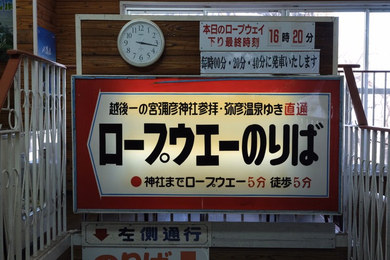A large red and white sign reads "越後の宮譜神社茅排・弥彦温泉ゆき直通 ロープウェイのりば" and "本日のロープウェイ 下り最終時刻 16時20分".