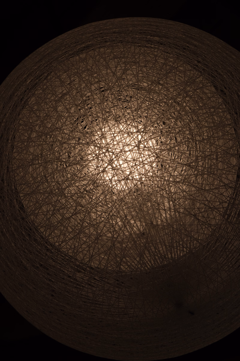 A dark, spherical abstract image composed of numerous intersecting, fine lines creating a complex, web-like pattern.