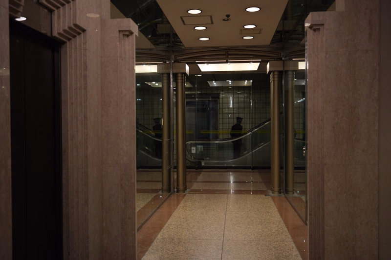 A view down a modern interior lobby featuring a glass-enclosed escalator surrounded by polished stone columns.