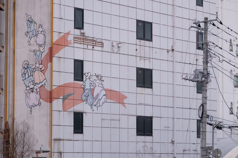 A large white building features a colorful mural depicting several cartoon characters in a group scene.
