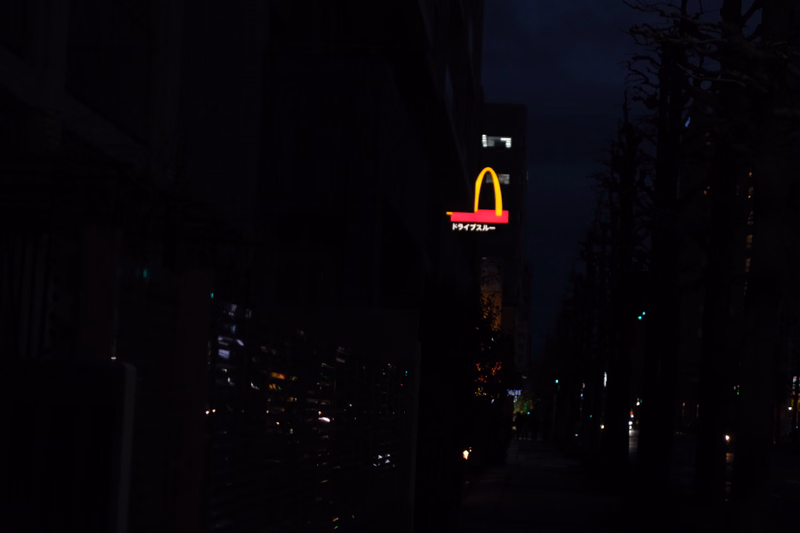 A bright yellow McDonald's 'M' sign with Japanese text reading "ドライブスルー" is visible at night.