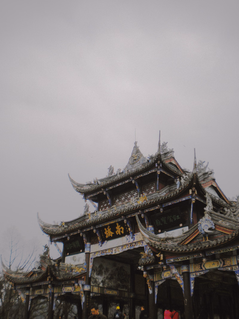 A large, traditional Chinese temple building with ornate, tiered roofs is visible under a bright, overcast sky.